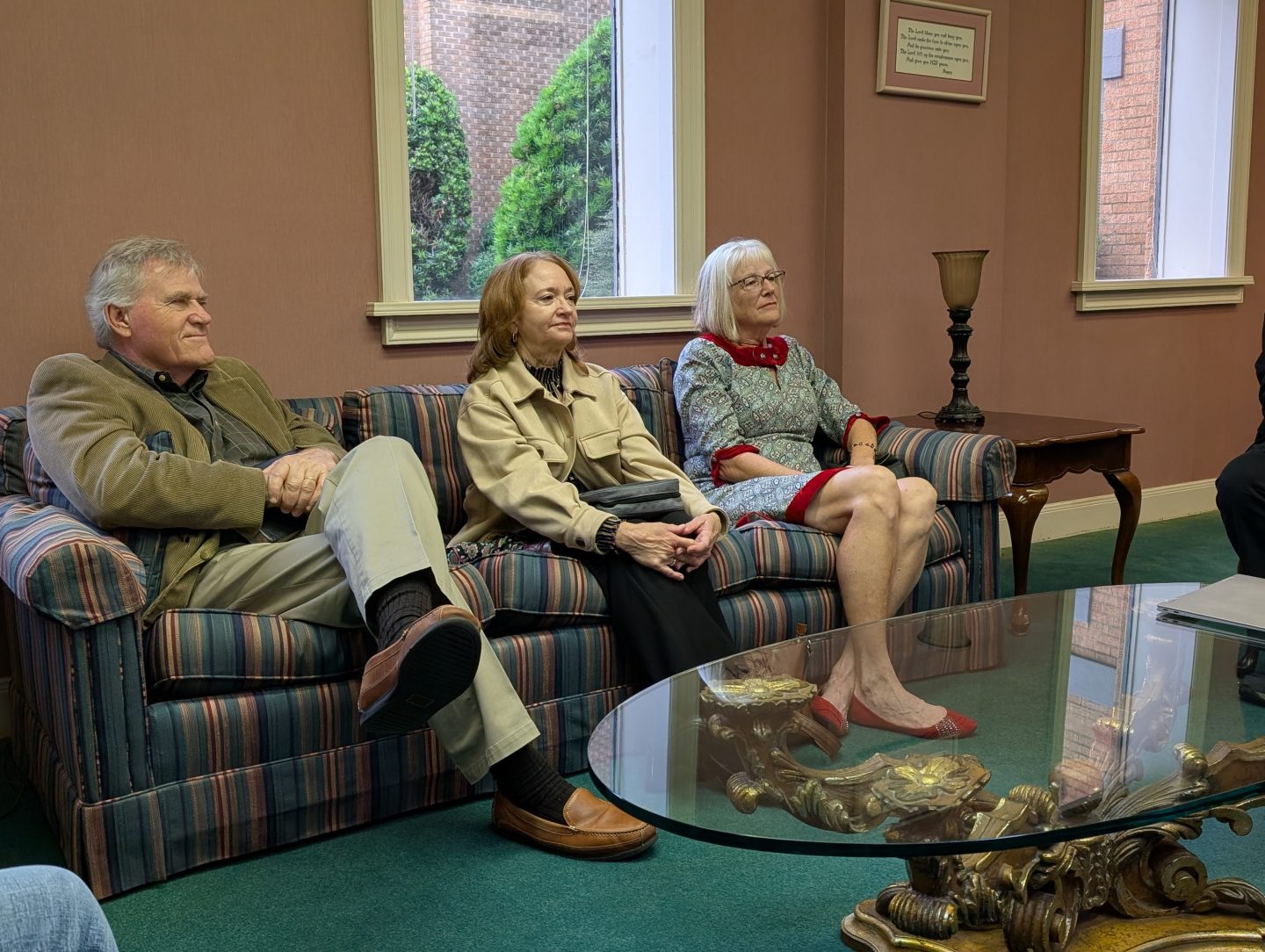photo of three adults, one male and two females, sitting on a couch with a table in the foreground. They are looking attentively to someone on the right but out of the photo.