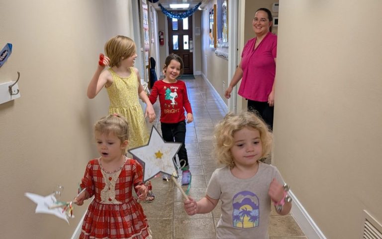 Children in the hallway in parade formation, leading child holds a star and the second girl is jumping up with excitement.