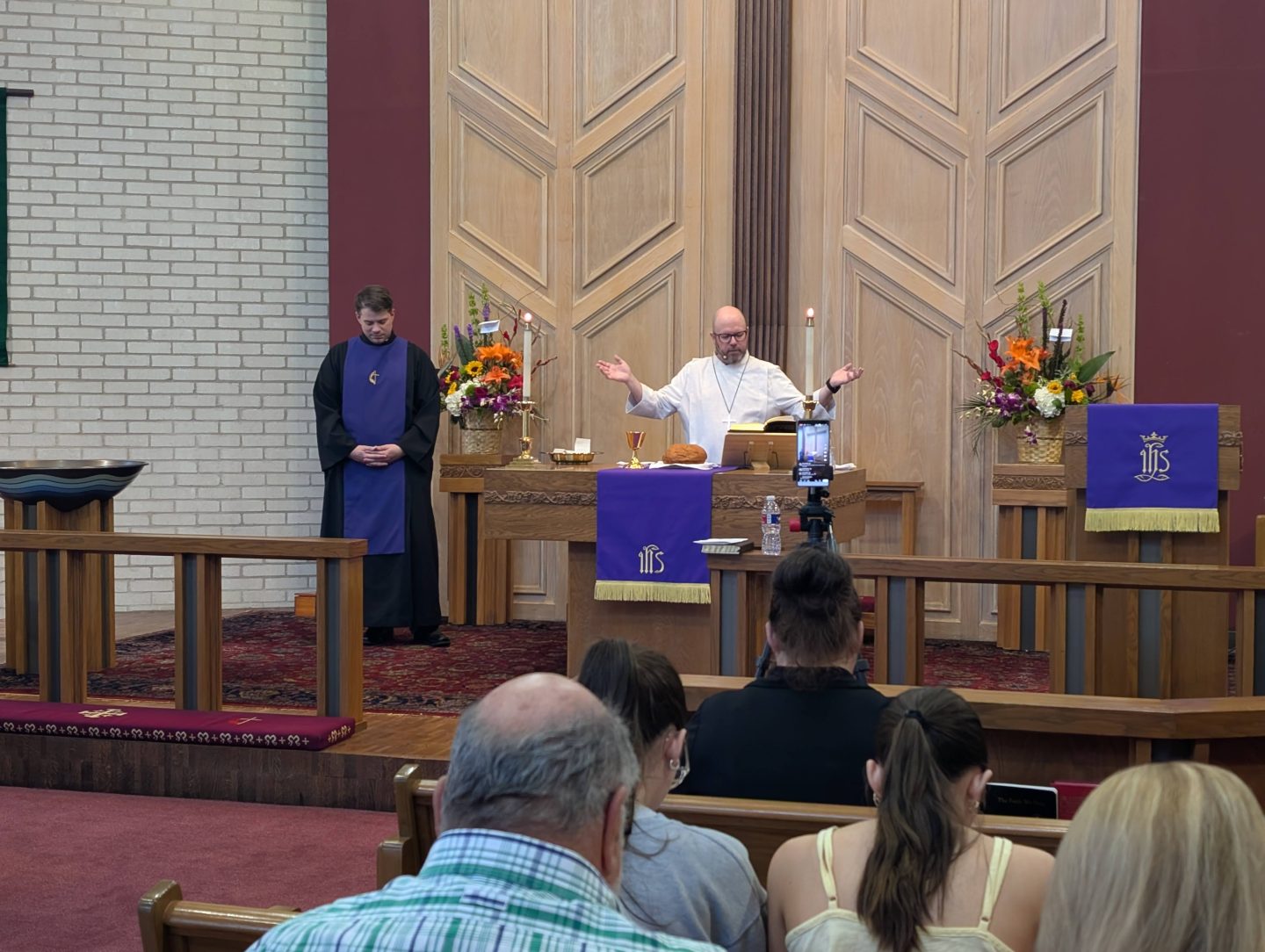 photo during worship in the sanctuary. Congregation with heads bowed and pastors with hands raised in prayer.